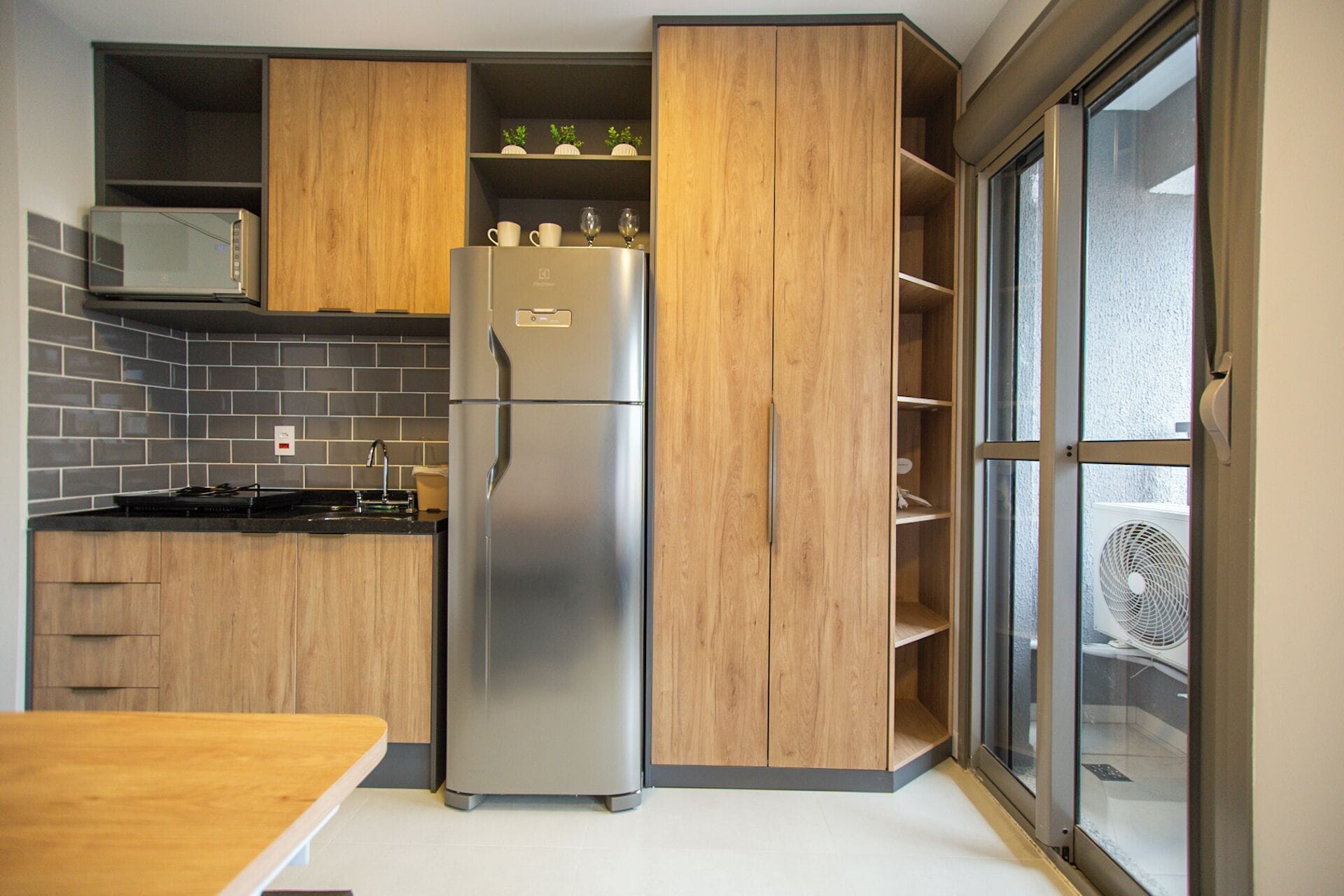 Eine Küche mit Holzausstattung, einem Edelstahlkühlschrank, einer Mikrowelle und einem Fenster mit Ventilator.