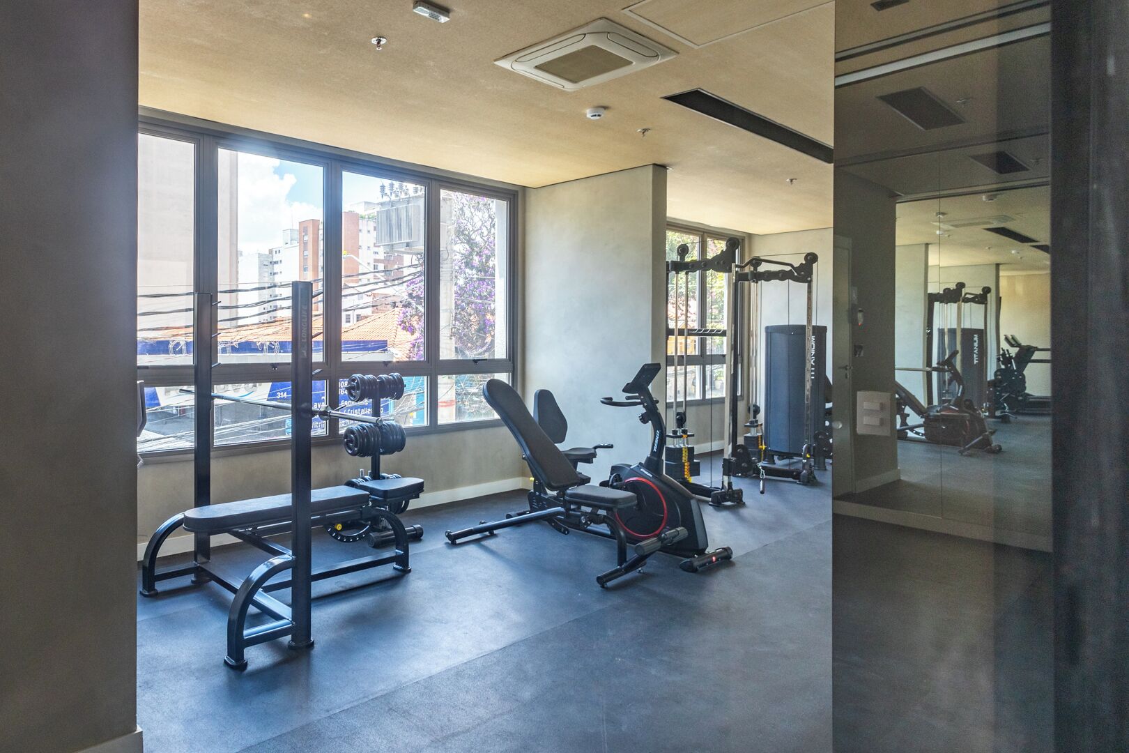Une salle de sport équipée de matériel d’exercice, dotée de grandes fenêtres et offrant une vue sur les bâtiments environnants.