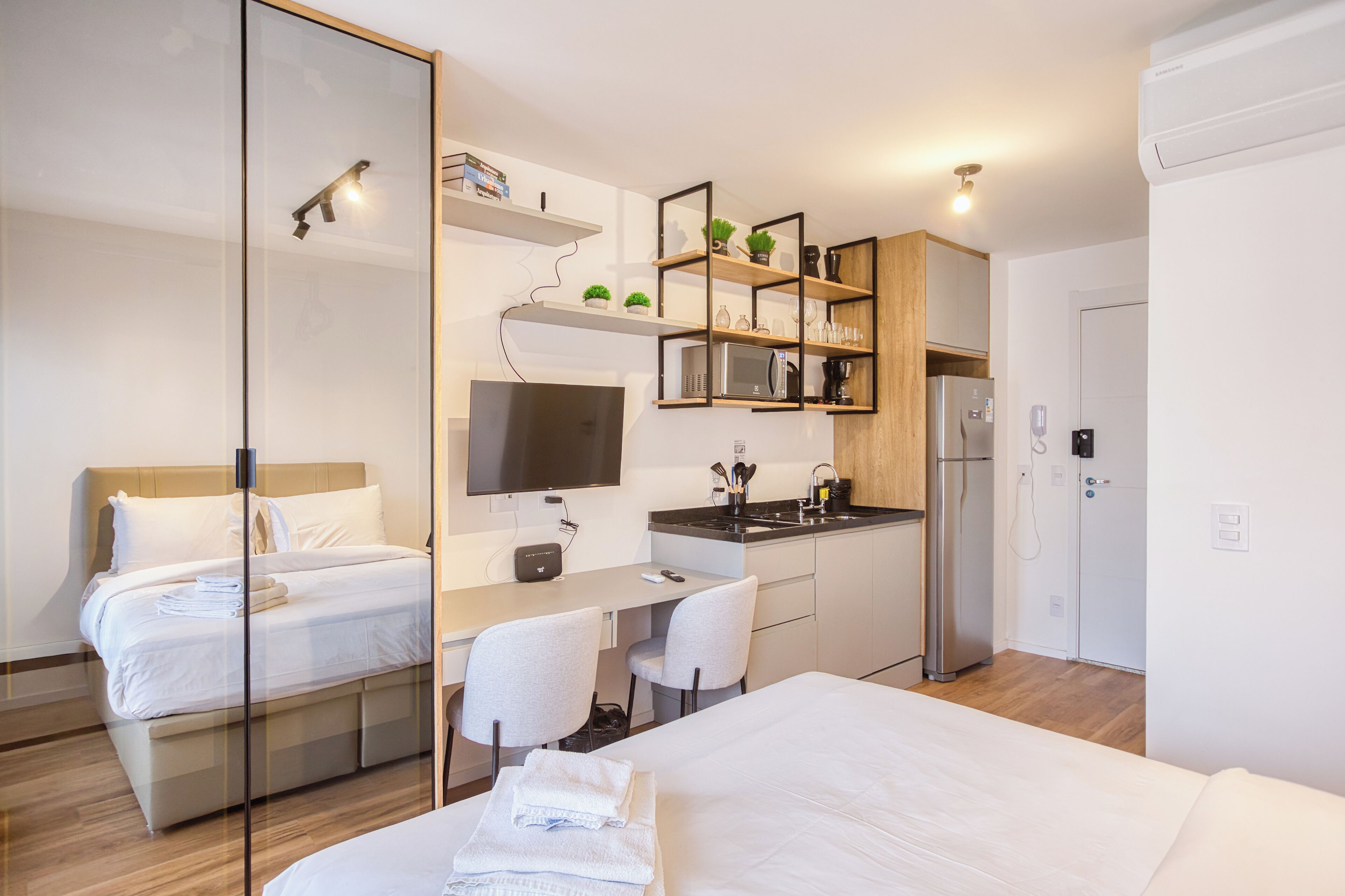 Ein modernes Hotelzimmer mit einem Bett, einem Schreibtisch, einem Stuhl, einem Fernseher, einer Mikrowelle, einem Kühlschrank und einer kleinen Küchenzeile.