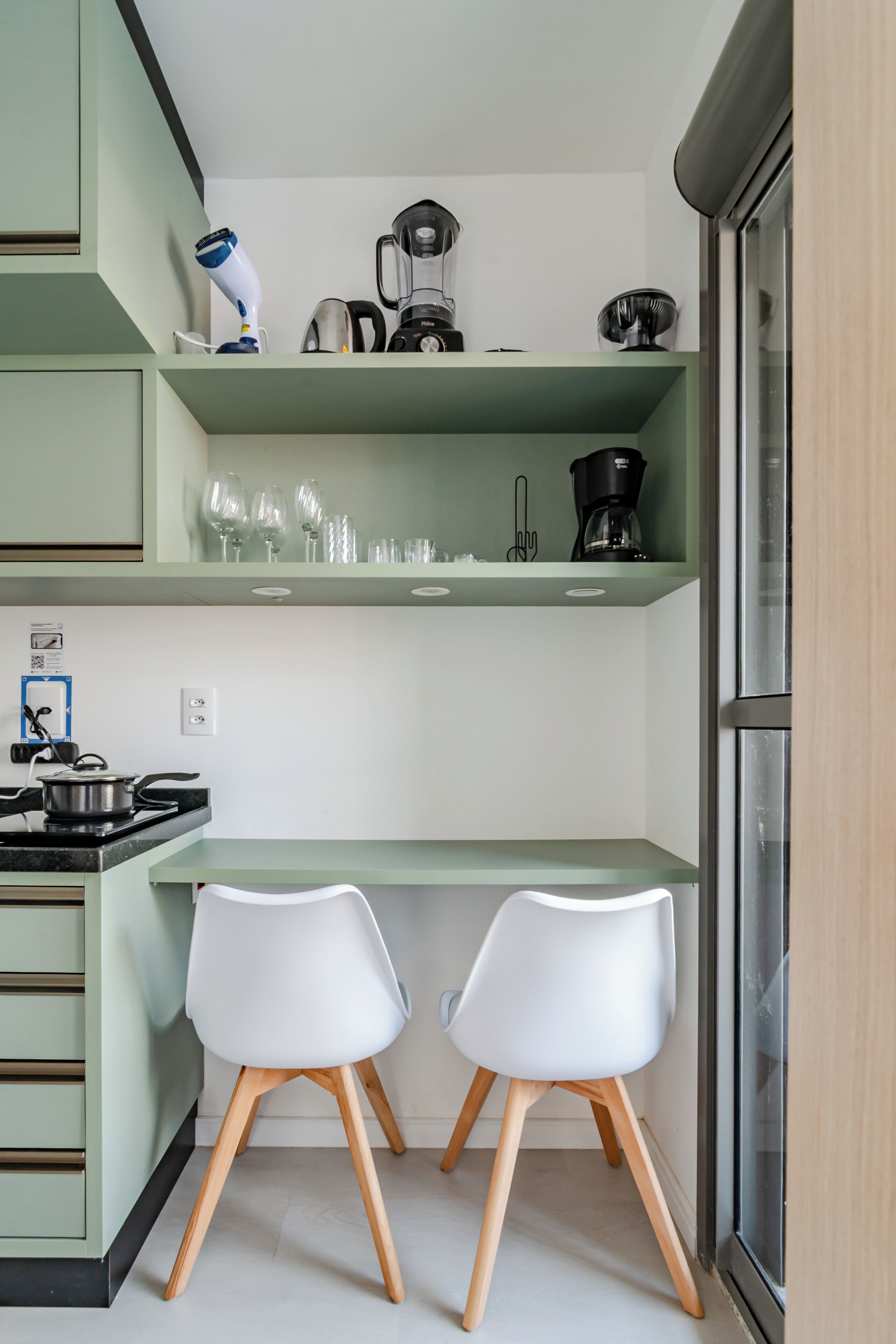 A compact kitchen with two white chairs, a stove, and various appliances on shelves.