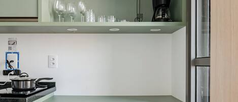 A compact kitchen with two white chairs, a stove, and various appliances on shelves.