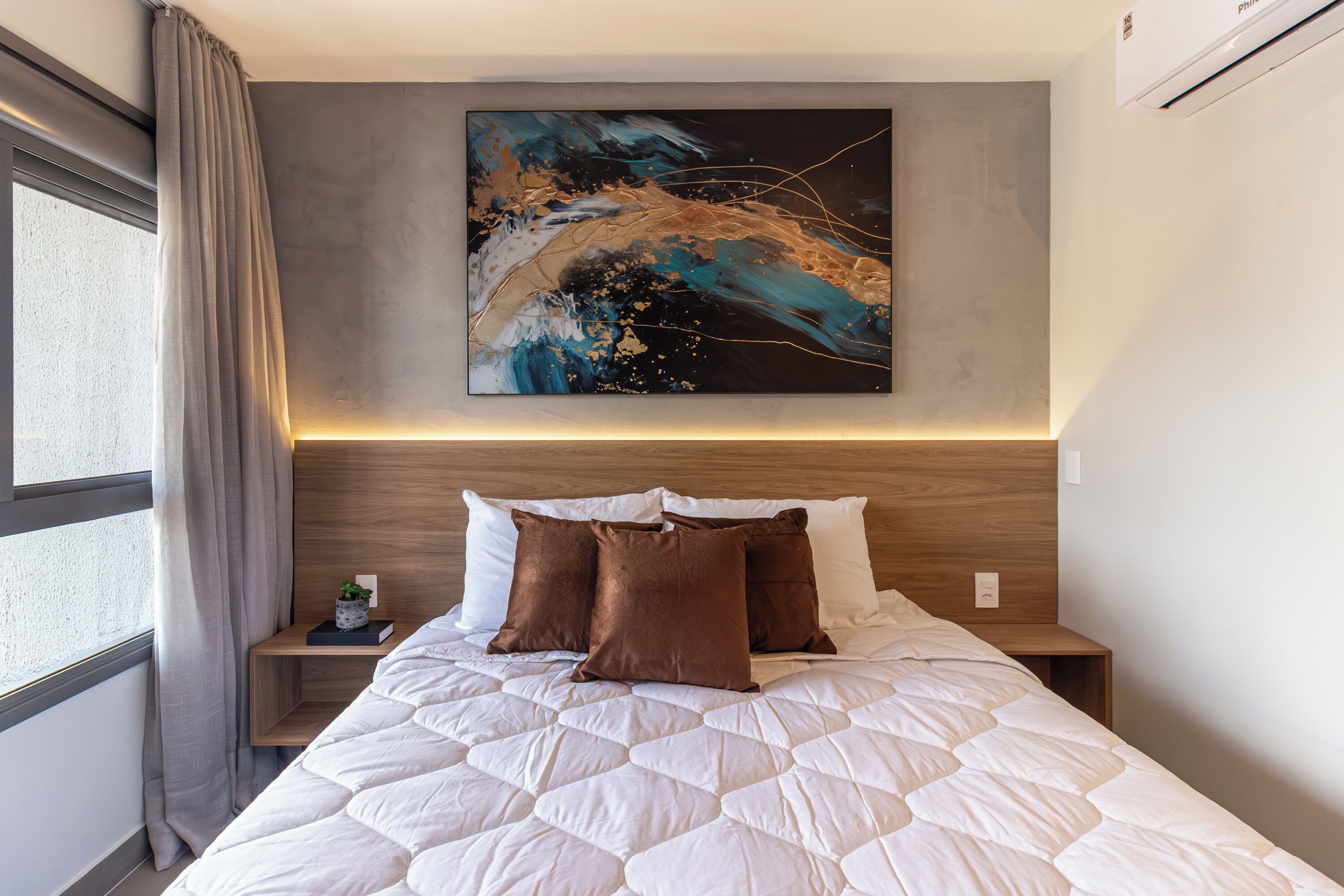 A hotel room with a bed, a nightstand, a wall-mounted painting, and a window with curtains.