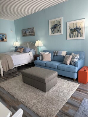 Un dormitorio con cama, sofá azul, reposapiés gris y mesita de noche con lámparas.