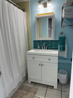 Un baño con lavamanos blanco, espejo, toallero y cortina de ducha.