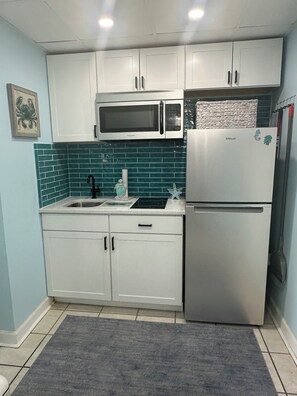 Una cocina con armarios blancos, un refrigerador de acero inoxidable, un microondas y un lavamanos con salpicadero color turquesa.
