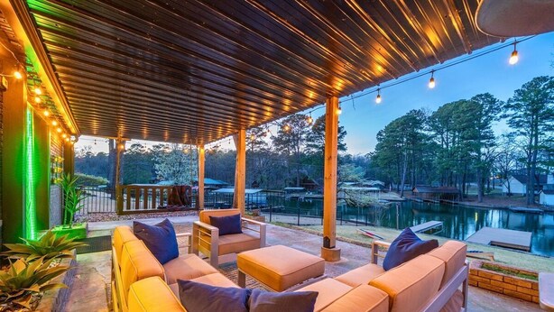 An outdoor seating area with sofas and tables, a wooden pergola, string lights, and a view of a body of water and trees. - Shadow Haven: Lakefront Dock & Boat Slip Retreat (Hot Springs)
