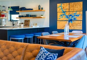 A modern kitchen with blue bar stools, a wooden dining table, and a map mural on the wall.