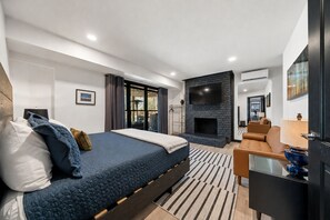 Une chambre moderne avec un grand lit, une cheminée, un téléviseur et un canapé.