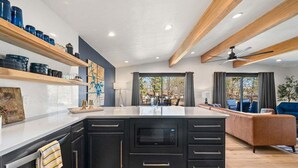 A modern kitchen with black cabinetry, a central island, and a dining area with a sofa. - Shadow Haven: Lakefront Dock & Boat Slip Retreat (Hot Springs)