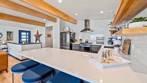 Een moderne keuken met een centraal eiland, barkrukken, roestvrijstalen apparatuur en houten balken.