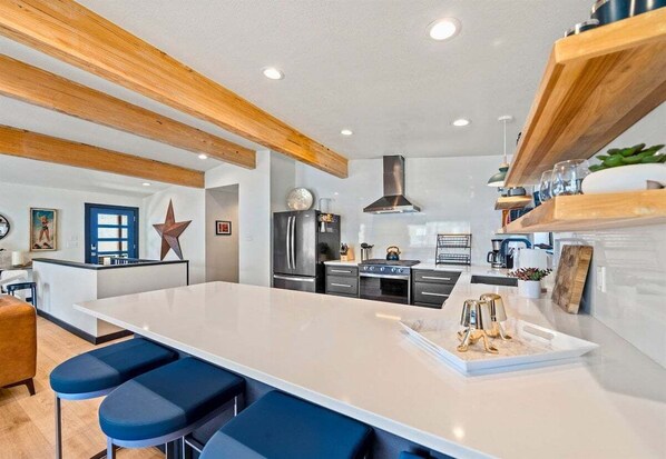 Een moderne keuken met een centraal eiland, barkrukken, roestvrijstalen apparatuur en houten balken.
