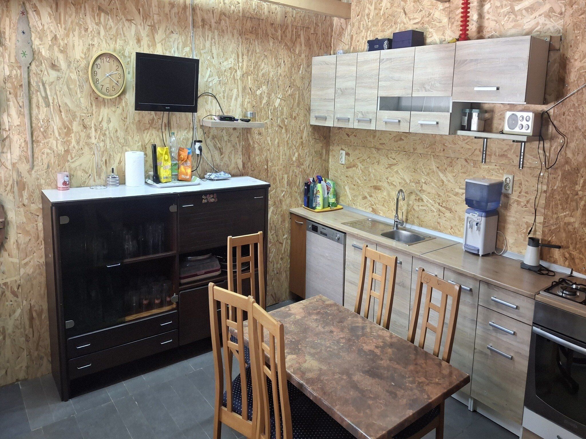 Una cocina compacta con un panel de madera, un refrigerador negro, una mesa de madera y un horno empotrado.