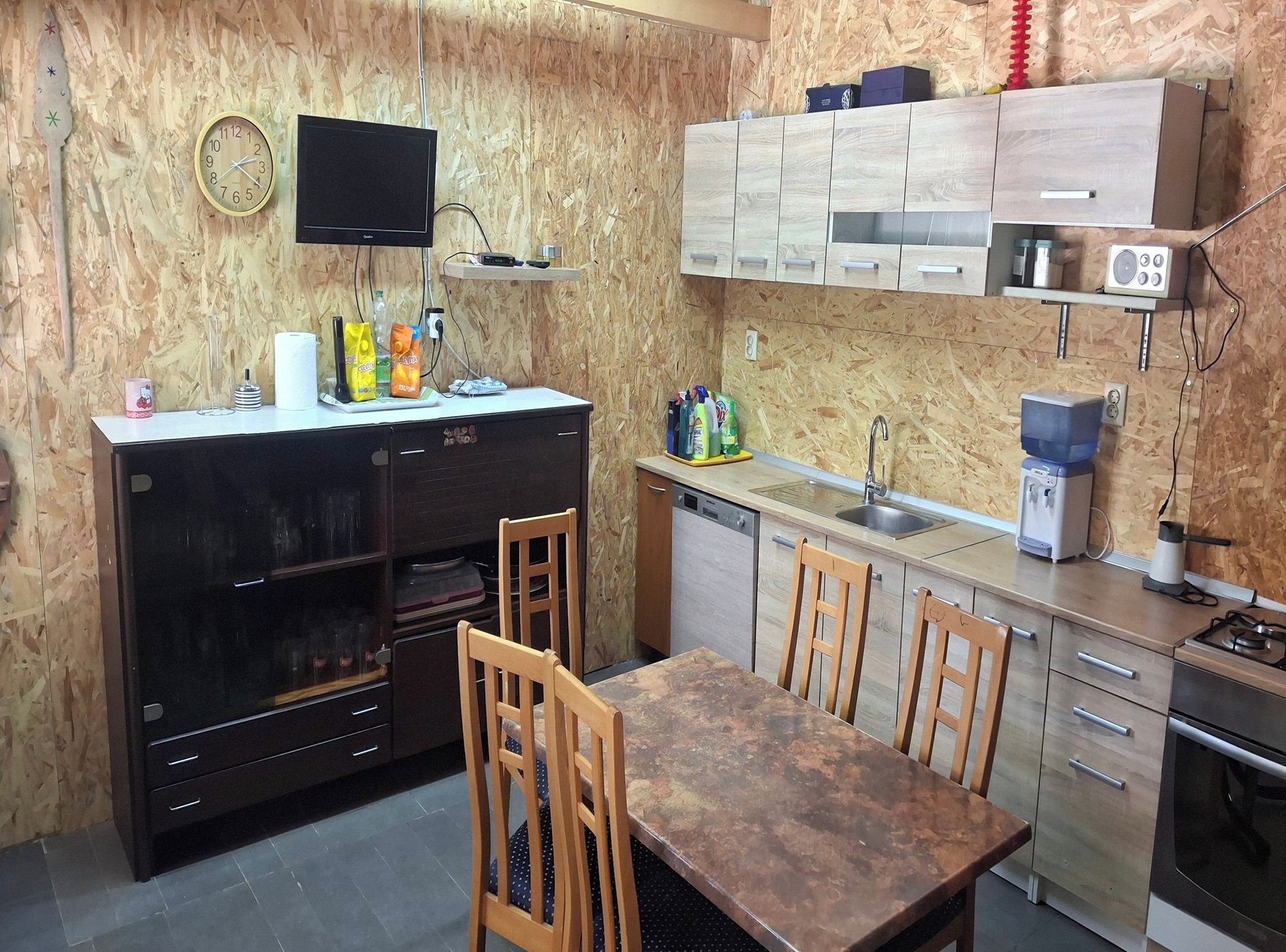 A compact kitchen with a dining table, chairs, a microwave, a sink, and a television mounted on the wall.