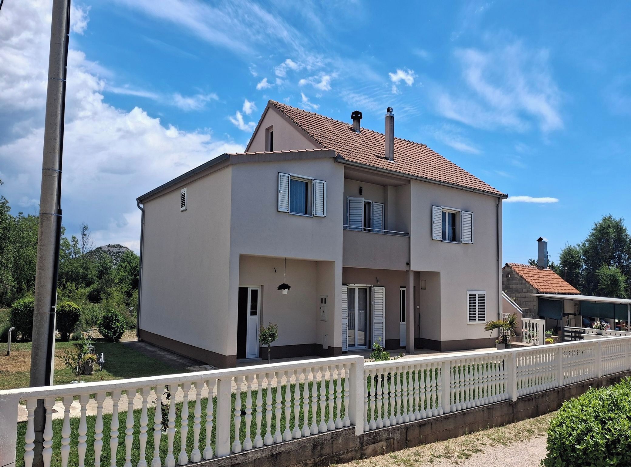 A two-story house with a tiled roof, a balcony, and a white fence.