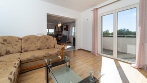 Un soggiorno moderno con divano, tavolino in vetro e vista su un balcone esterno tramite una porta scorrevole.