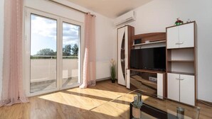 Un soggiorno moderno con una televisione a schermo piatto, mobili in legno e una porta scorrevole in vetro che dà su un balcone.