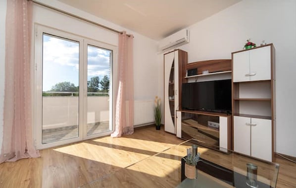A modern living room with a flat-screen TV, wooden cabinets, and a sliding glass door leading to a balcony. - Holiday Home Iva & Luca (Benkovac)