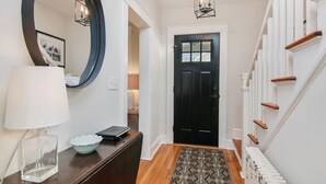 A hallway with a black door, a round mirror, a desk with a lamp, and a patterned rug. - Charming Walk to downtown Mystic Awaits Your Stay (Mystic)
