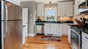 A modern kitchen with white cabinets, stainless steel appliances, and a wooden floor. - Charming Walk to downtown Mystic Awaits Your Stay (Mystic)