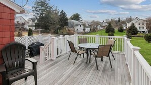 A wooden deck with a table and chairs, surrounded by white railings. - Charming Walk to downtown Mystic Awaits Your Stay (Mystic)
