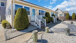 A single-story mobile home with a front porch, white railings, and a gravel driveway. - Professionally Managed | Walk to Beach (Seaside Heights)