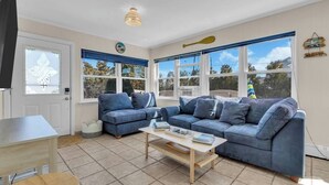 A living room with two blue sofas, a coffee table, and a TV. There are large windows with blinds, a door, and a ceiling light fixture. - Professionally Managed | Walk to Beach (Seaside Heights)