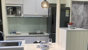 Een moderne keuken met witte kasten, een inbouwoven, een magnetron en een roestvrijstalen spoelbak. Er is een eethoek met een witte tafel en zwarte stoelen.