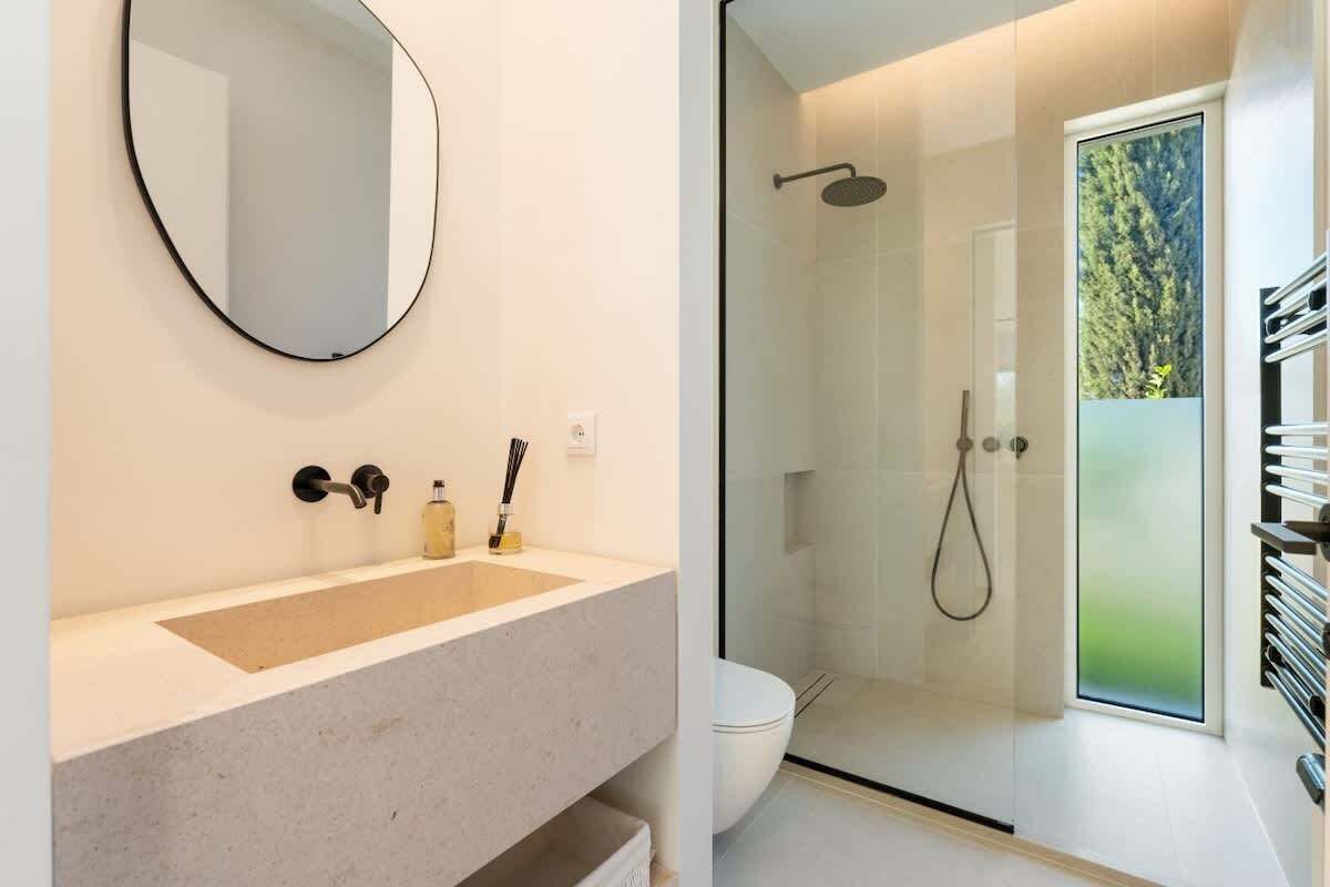Un baño moderno con un espejo grande, un lavamanos color beige y una ducha con cerramiento de vidrio.