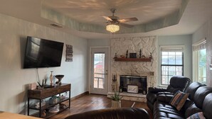 A living room with a fireplace, a ceiling fan, a TV, and a leather couch. - The lake house (Murchison)