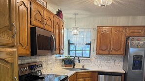 A kitchen with wooden cabinets, stainless steel appliances, a chandelier, and a window with sheer curtains. - The lake house (Murchison)