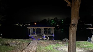 A gazebo with a stone pathway leading to it, surrounded by trees and a body of water in the background. - The lake house (Murchison)