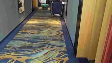 A hotel hallway with patterned carpet, a trash bin, and a luggage cart.