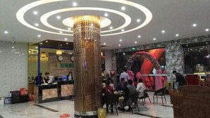 Un hall d’hôtel doté d’une colonne centrale, d’un comptoir d’accueil et d’un espace détente où des personnes prennent leur repas.