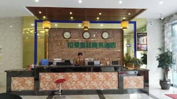 A hotel reception desk with a marble counter, a clock, and a potted plant.