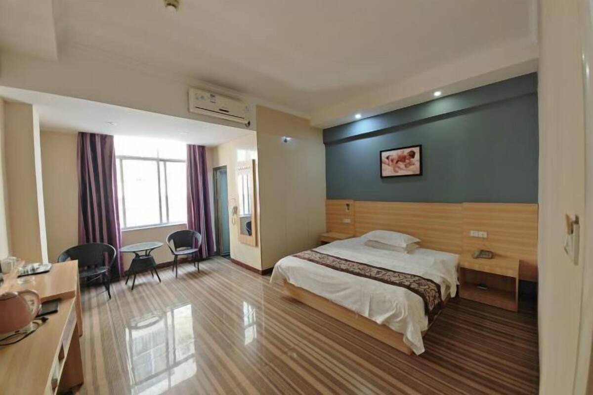 Habitación de hotel con cama, escritorio, silla, una mesita y ventana con cortinas.