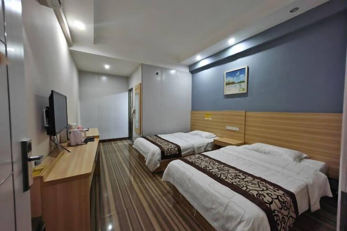 Una habitación de hotel con dos camas, un escritorio con televisor y un cuadro en la pared.