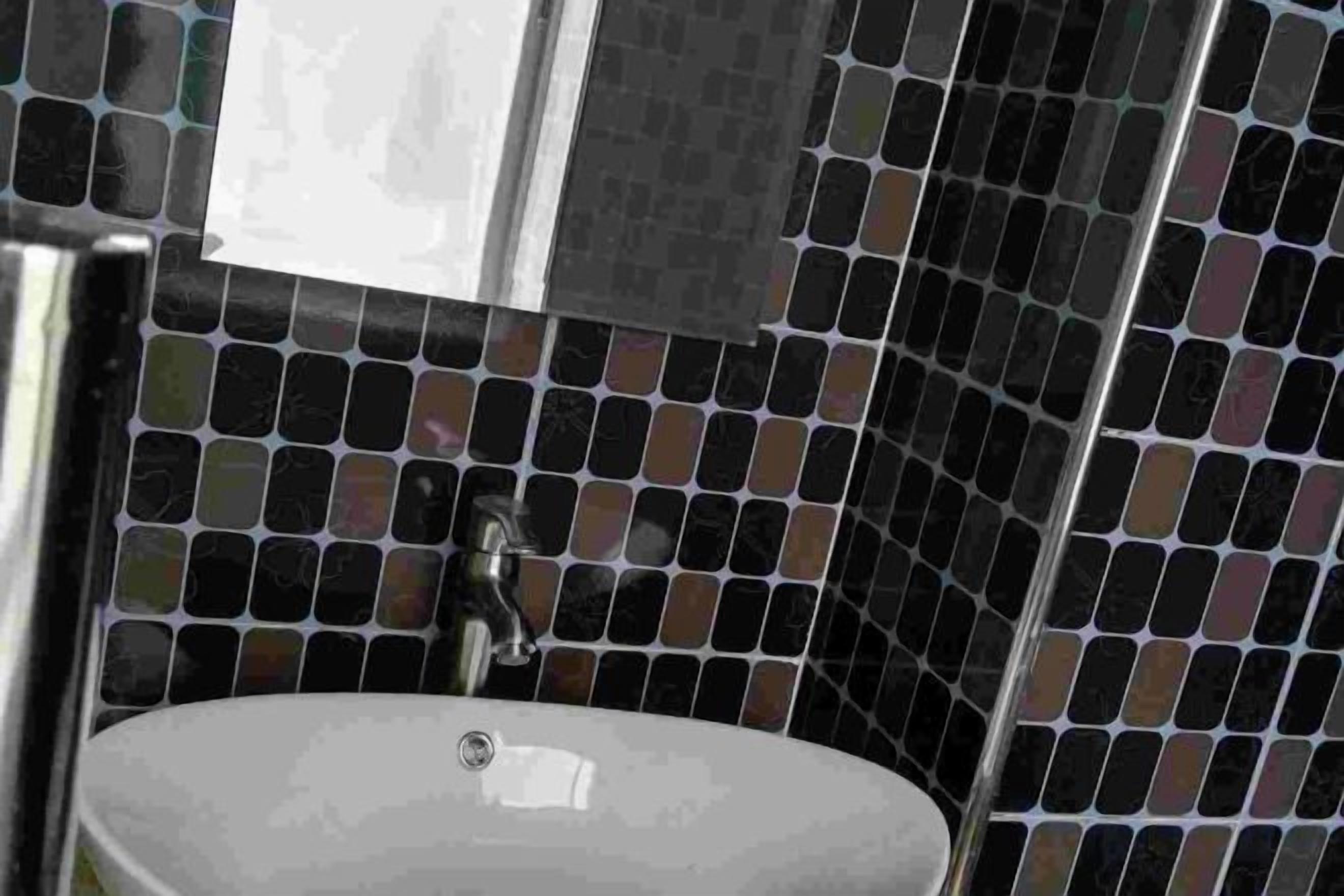 A bathroom with a white sink, a mirror, and black and brown mosaic tiles on the walls.