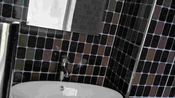 A bathroom with a white sink, a mirror, and black and brown mosaic tiles on the walls.