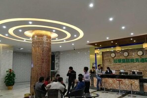 Eine Hotelhalle mit einer Rezeption, einer großen Säule und einer Gruppe von Personen.