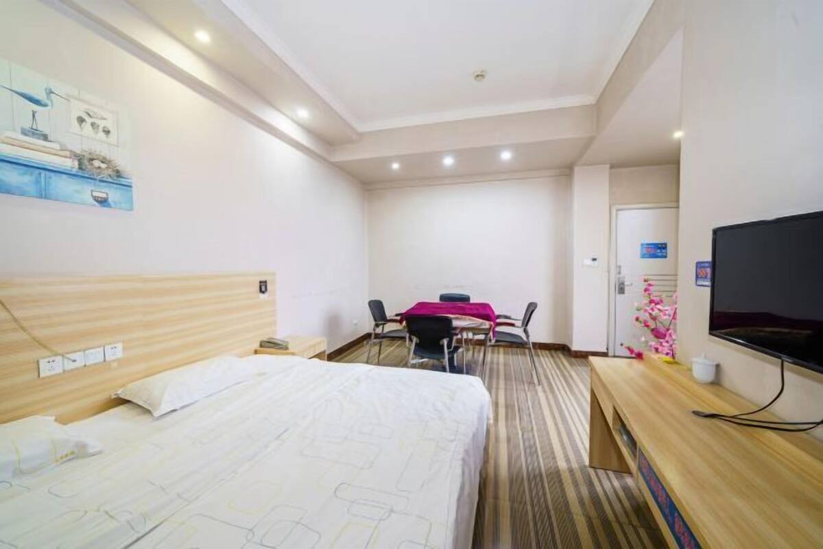 Habitación de hotel con cama, escritorio, silla, televisor y una pequeña mesa con mantel rosa.