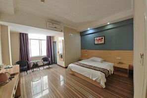 Habitación de hotel con cama, mesita de noche y escritorio con sillas. Cuenta con una ventana con cortinas, aire acondicionado instalado en la pared y un cuadro enmarcado.
