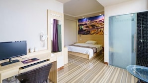 Une chambre d’hôtel comprenant un lit, un bureau avec un ordinateur, une chaise, une douche et un mur orné d’une fresque représentant un paysage urbain.