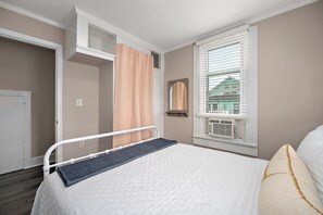 A bedroom with a bed, a window with blinds, a view of a building outside, and a door to another room. - Coastal-Chic · Pool, Bay View & Balcony·Walk2Beach (Ocean City)