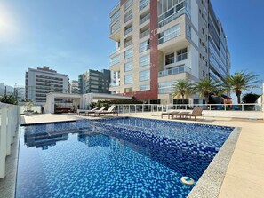 A swimming pool with a tiled edge, surrounded by lounge chairs and a building with multiple balconies. - Cobertura com Jacuzzi em Palmas  (Governador Celso Ramos)