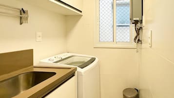 Uma lavanderia compacta com máquina de lavar, pia e lixeira.