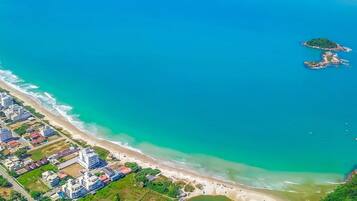 Vista aérea de una zona costera con una playa, una pequeña isla y una área residencial con edificios.
