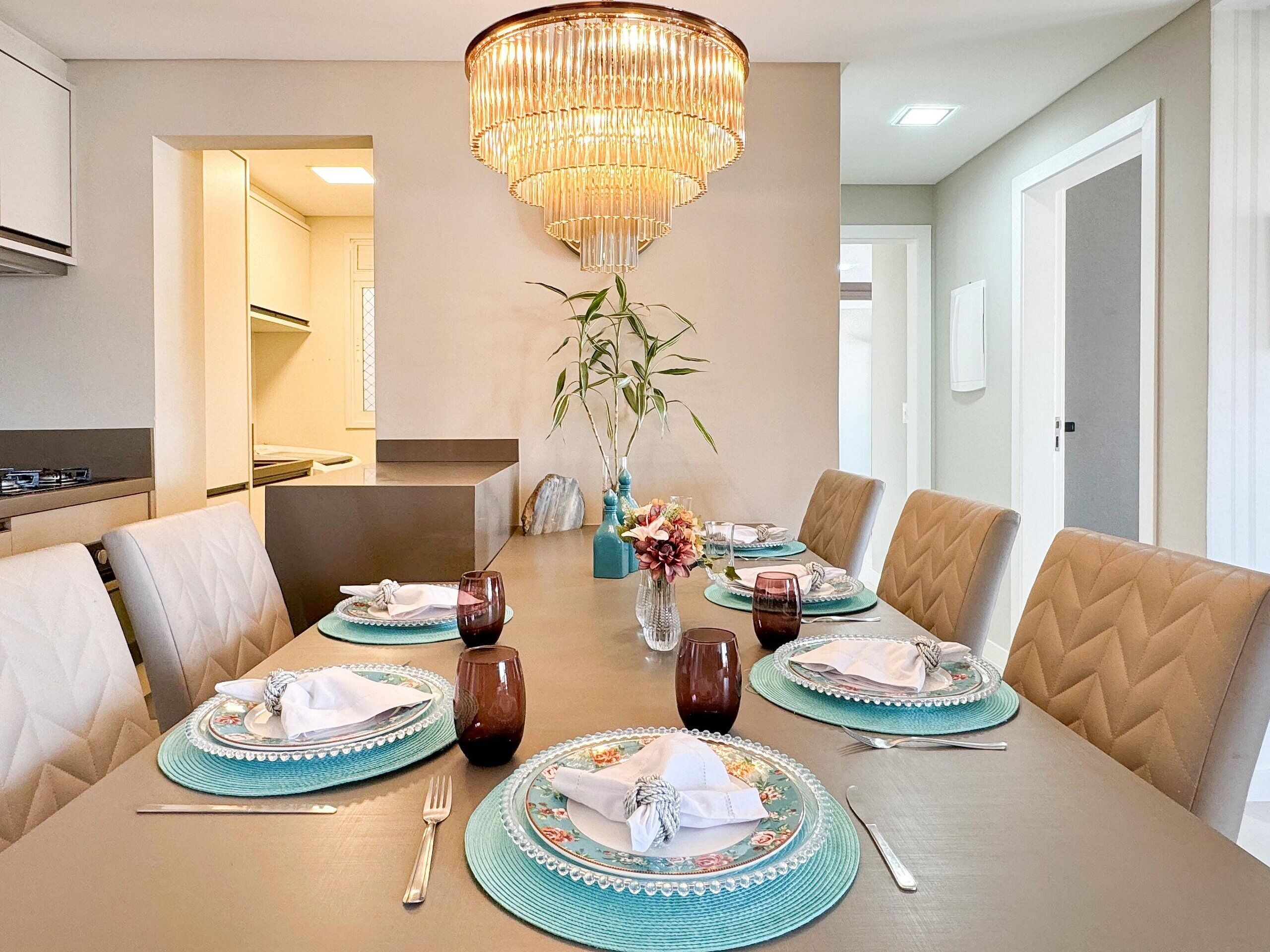 A dining area with a chandelier, a vase with flowers, and a table set for six.