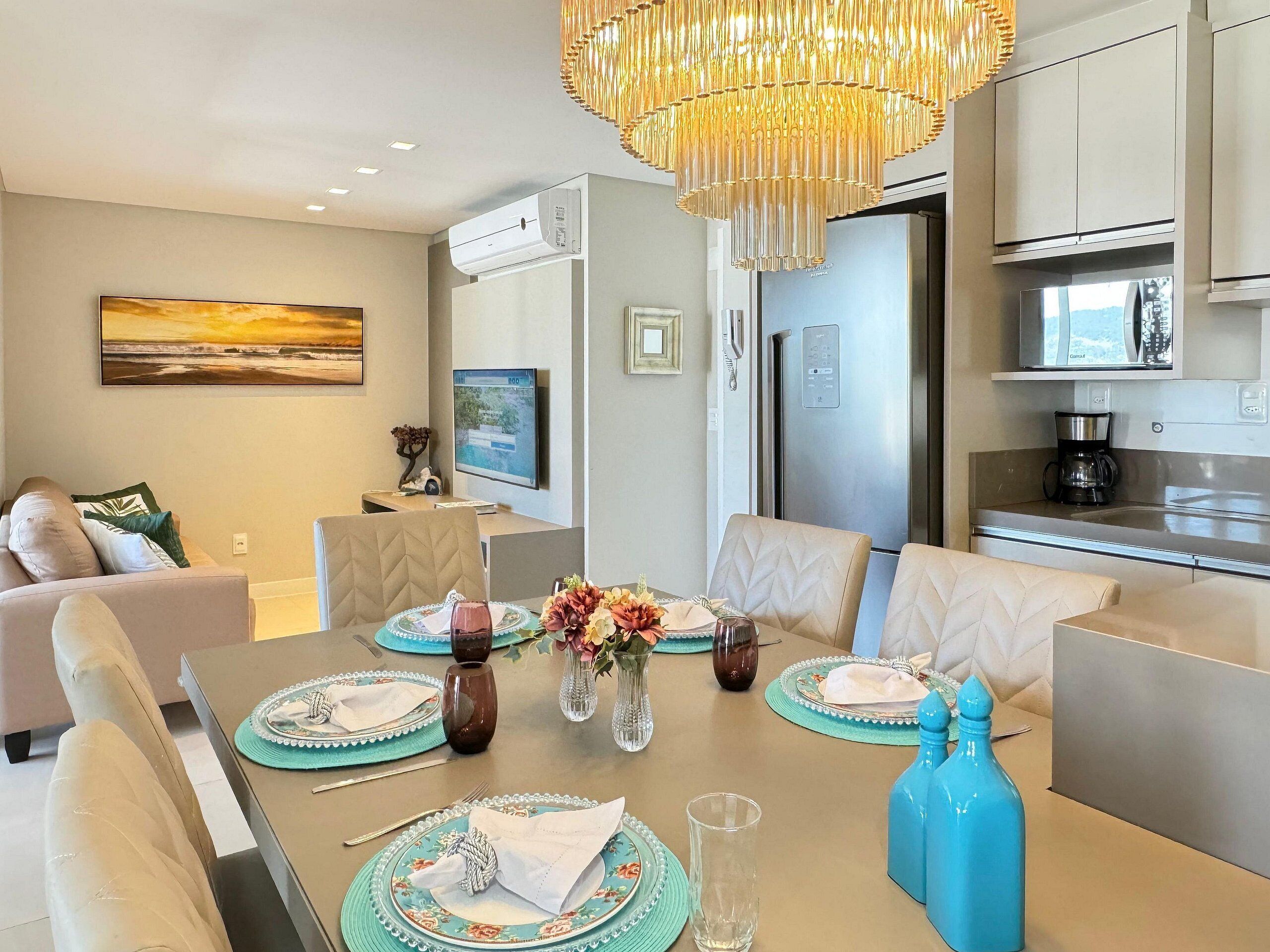 A modern dining area with a chandelier, a flat-screen TV, and a refrigerator.