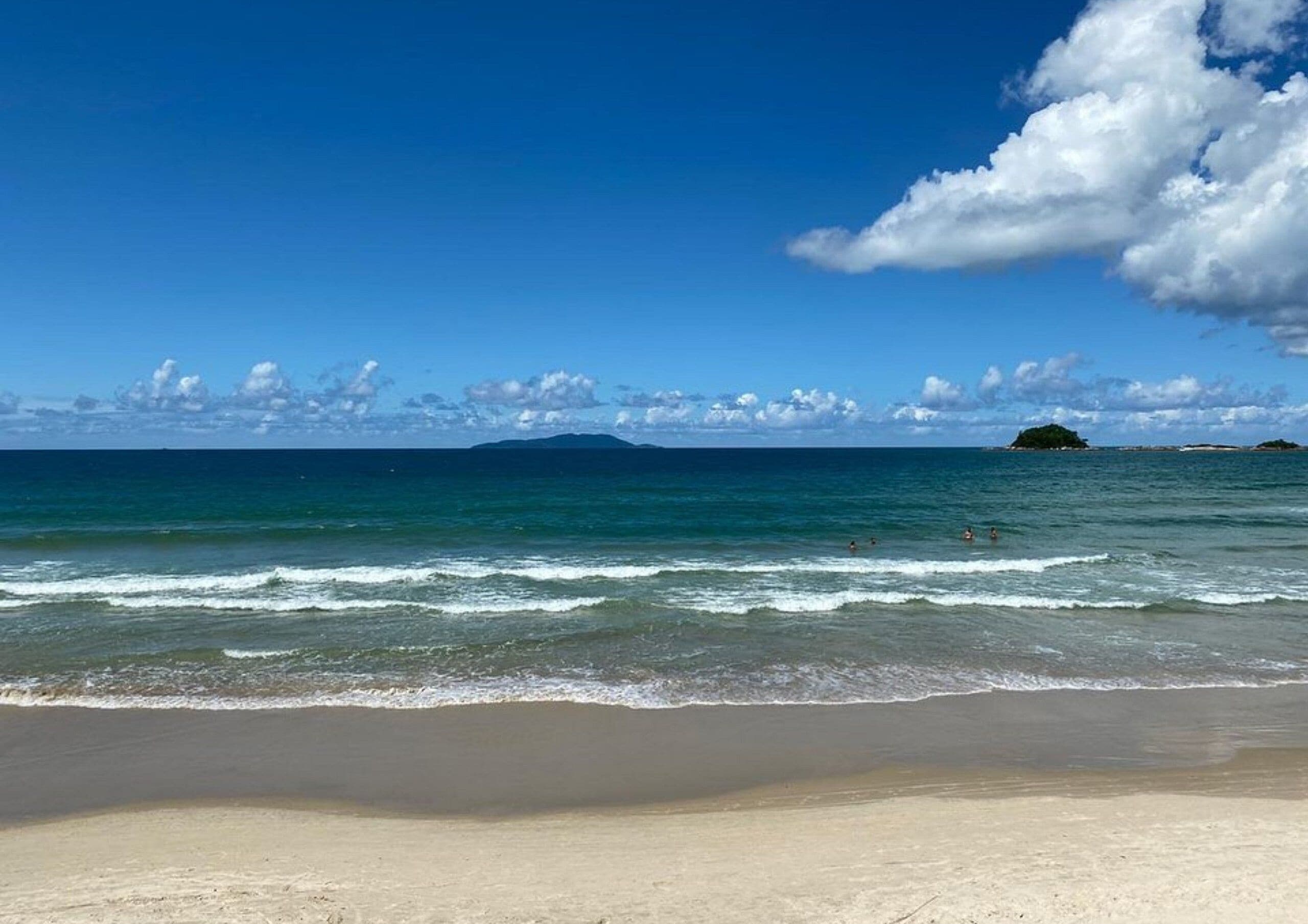 A beach with clear blue water, waves, and distant islands.