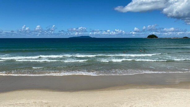 Una playa con agua azul cristalina, una orilla arenosa e islas a lo lejos.